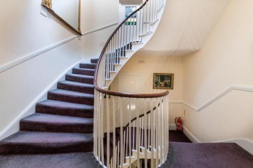 a winding staircase in a home with white walls and purple carpet at The George Hotel in Battle