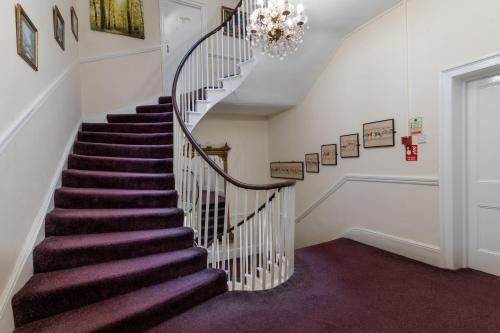 a staircase in a home with purple carpet and a chandelier at The George Hotel in Battle
