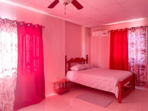 a bedroom with pink walls and a bed with red curtains at Apartment at Trincity Central Road in Port-of-Spain