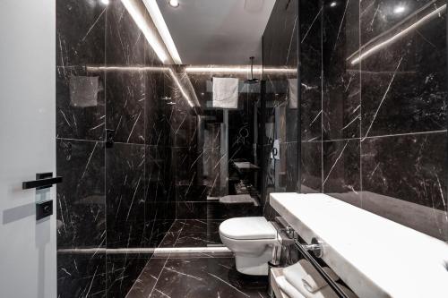 a black tiled bathroom with a toilet and a sink at The Grandeur Hotel in Batumi