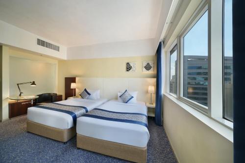 two beds in a hotel room with a large window at Kingsgate Hotel by Millennium in Abu Dhabi