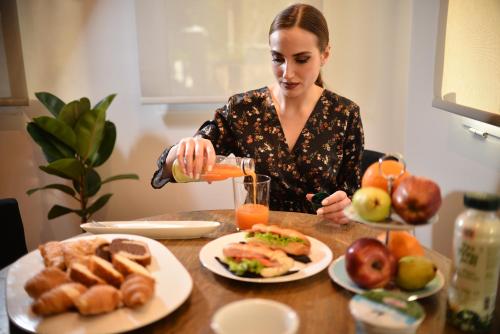 Uma mulher a deitar um copo de sumo de laranja sobre uma mesa de comida. em Anixi Hotel by AP em Atenas