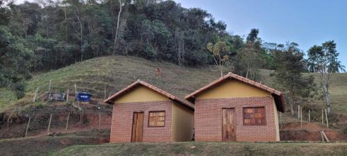 een klein huis met een heuvel op de achtergrond bij Pousada Fazenda e Pesqueiro Chalé da serra in Conceição da Ibitipoca