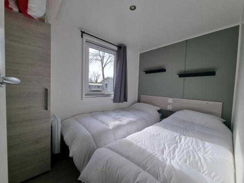 two beds in a small room with a window at Mobil home 2 chambres Camping **** (507) in Saint-Jean-de-Monts