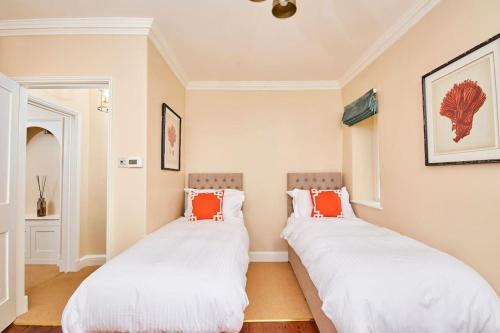 two beds in a room with white and orange pillows at North Lodge - 17th Century Gate Cottage at Hassop Hall in Hassop