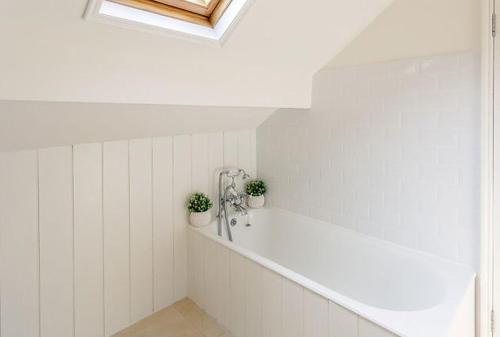 a white bathroom with two potted plants on a ledge at North Lodge - 17th Century Gate Cottage at Hassop Hall in Hassop