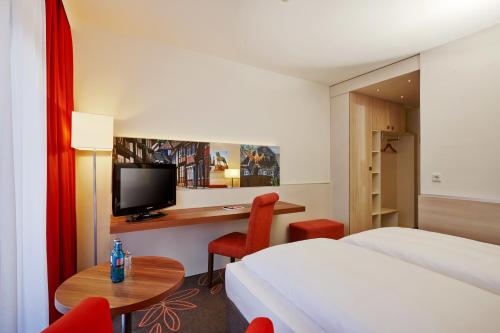 a hotel room with a bed and a desk with a tv at H+ Hotel Goslar in Goslar