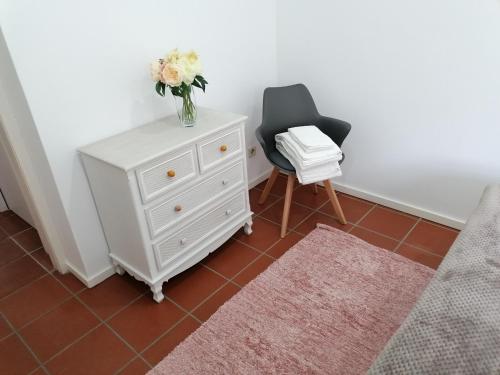 uma cómoda branca com um vaso de flores e uma cadeira em Casa da Bichaca em Castelo de Paiva