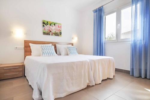 1 dormitorio con 1 cama blanca grande y cortinas azules en Villa Verano en Cala Galdana
