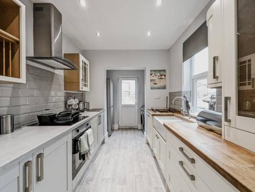 a large kitchen with white cabinets and wooden floors at Derrington House - By Sigma Stays in Crewe