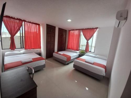 two beds in a room with red curtains and windows at HOTEL DIAMANTE in Santo Domingo de los Colorados