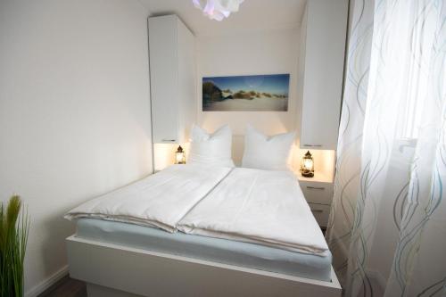 ein weißes Schlafzimmer mit einem weißen Bett und weißen Kissen in der Unterkunft Am Sahlenburger Strand - Wohnung 4 in Cuxhaven