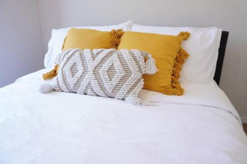 1 cama con sábanas blancas y almohadas amarillas en ViQi Two bedroom apartment front of century walk Including Premium NETFLIX & Prime AMAZON with 75 INCH TV, en Glen Waverley