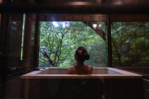 a woman sitting in a bath tub in a forest at Treeful Treehouse Sustainable Resort Okinawa in Nago