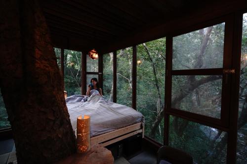 Una mujer en una cama en una habitación con ventanas en Treeful Treehouse Sustainable Resort, en Nago