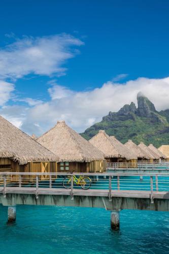 a pier with huts on the water with a mountain at The St. Regis Bora Bora Resort in Bora Bora