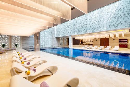 a large swimming pool with white lounge chairs and a swimming pool at Al Messila, A Luxury Collection Resort & Spa, Doha in Doha