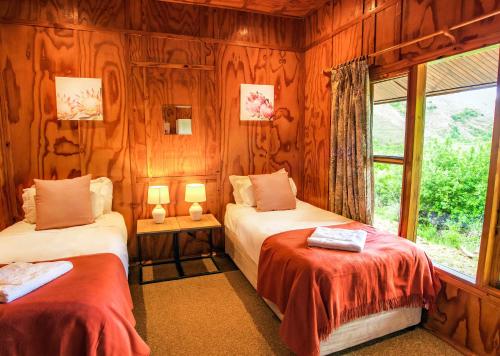 2 Betten in einem Zimmer mit Holzwänden und einem Fenster in der Unterkunft Highland Run Fly Fishing Estate by Dream Resorts in Lydenburg