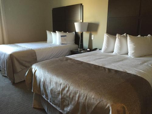 two beds in a hotel room with white sheets at Baymont by Wyndham College Station in College Station