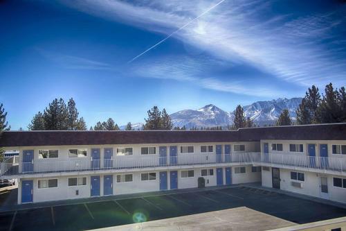 a building with a parking lot and mountains in the background at Motel 6-Mammoth Lakes, CA in Mammoth Lakes