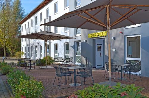 een patio met tafels, stoelen en parasols voor een gebouw bij B&B Hotel Düsseldorf-Ratingen in Ratingen