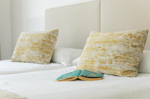 a book sitting on top of a bed with pillows at Hotel d'Or in Cala d´Or