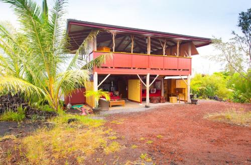 a red and yellow house with a palm tree at THE MAGICAL LAVA TEMPLE with EPIC Volcano Views! in Kehena