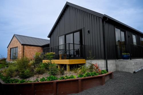 a black house with a garden in front of it at Piwakawaka Suite in Balclutha