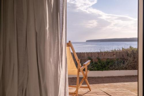 a chair sitting on a balcony looking out at the ocean at Hostal Aigua Clara in Playa Migjorn