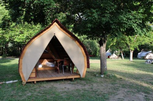 una pequeña tienda en un campo con un árbol en Habitat Créateur - Hébergements insolites au camping municipal "Les Ecureuils", en Recoubeau