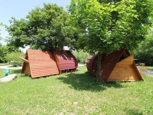 two small buildings sitting in the grass next to a tree at Habitat Créateur - Hébergements insolites au camping municipal "Les Ecureuils" in Recoubeau