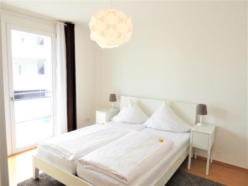 a white bedroom with a bed and a large window at Braviscasa - Ferienresidenz Stadttor Endingen in Endingen