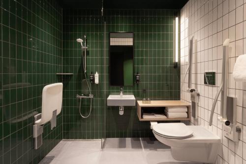 a green tiled bathroom with a toilet and a sink at ibis Styles Copenhagen Orestad in Copenhagen