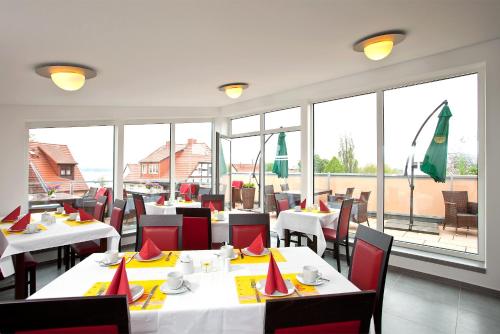 un restaurante con mesas blancas, sillas rojas y ventanas en Müritzperle en Waren