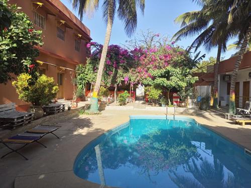 a swimming pool in front of a building with palm trees at Guesthouse Dalal ak Jàmm in Mbour