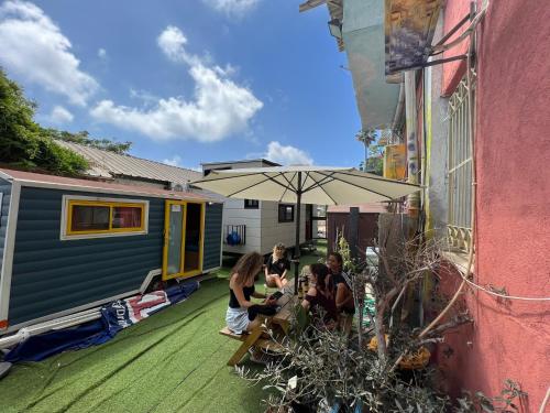 a group of people sitting under an umbrella next to a trailer at Roger's Hostel Tel Aviv (age 18-45) in Tel Aviv