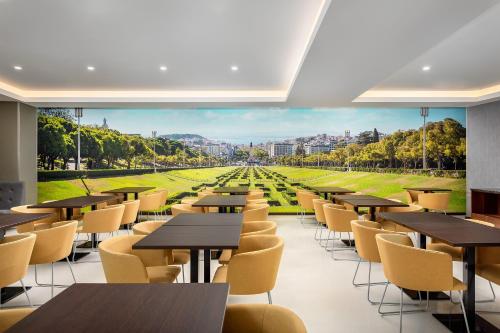 a cafeteria with tables and chairs and a view of a park at Empire Marquês Hotel in Lisbon