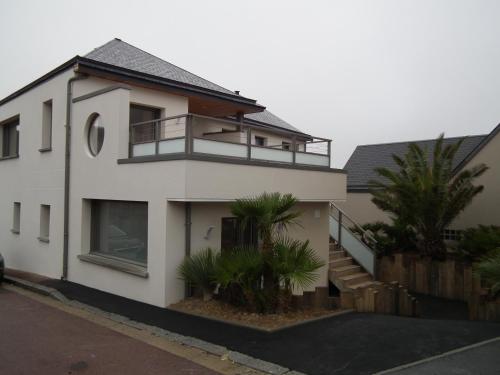 a white house with a balcony and palm trees at Les Maisons de Louise in Pirou