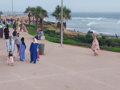 a group of people walking down a sidewalk near the beach at Appartement youssef in Agadir