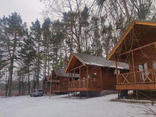 una cabaña de madera con un coche aparcado en la nieve en Kujanki - domki z widokiem na jezioro, en Zakrzewo