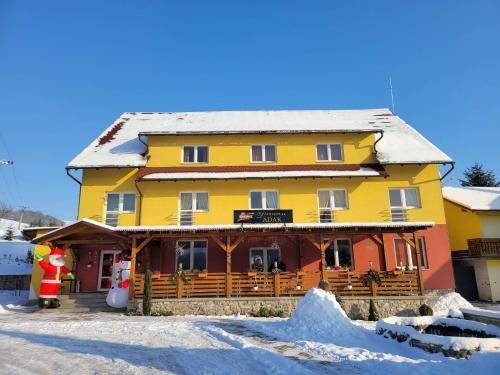 a yellow and orange building in the snow at Penzion Adak in Párnica