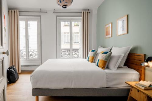 une chambre avec un grand lit blanc avec des oreillers dans l'établissement Edgar Suites Martyrs - Lebas, à Paris