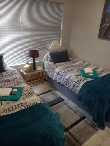 a bedroom with two beds and a table with a lamp at Chardonnay Holiday Apartment in Jeffreys Bay