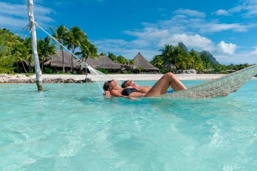 a woman in a hammock in the water at a resort at The St. Regis Bora Bora Resort in Bora Bora