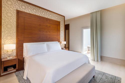 a bedroom with a large white bed and a wooden headboard at Al Messila, A Luxury Collection Resort & Spa, Doha in Doha