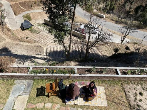 two people sitting on the ground in the grass at Francolin Lodge-Farmstay @ Darima in Mukteswar