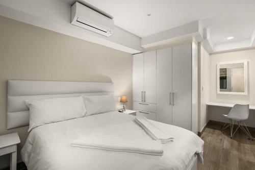 a white bedroom with a bed and a desk and a chair at The Regency Apartments in Pretoria