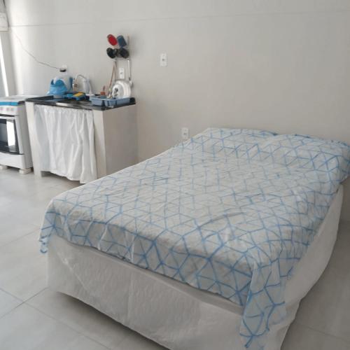 a bed with a blue and white comforter in a room at Edícula no centro de VR in Volta Redonda