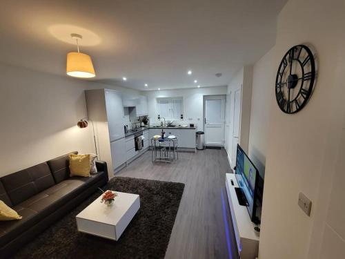 a living room with a couch and a table and a clock at New build home with WI-FI, Smart TV, dedicated office floor, large terrace and Free parking in Milton Keynes