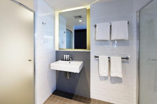La salle de bains blanche est pourvue d'un lavabo et d'un miroir. dans l'établissement Alpha Mosaic Hotel Fortitude Valley Brisbane, à Brisbane